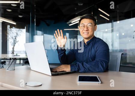 Portrait d'un jeune élégant programmeur asiatique travaillant au bureau à partir d'un ordinateur portable. Souriant en toute confiance et regardant l'appareil photo. Banque D'Images