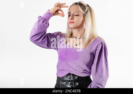 Jeune femme blonde portant un chemisier à côtes lilas isolé sur fond blanc yeux fermés les doigts du bras montrent un geste gastronomique. Lèvres en sachet. Essayer délicieux Banque D'Images