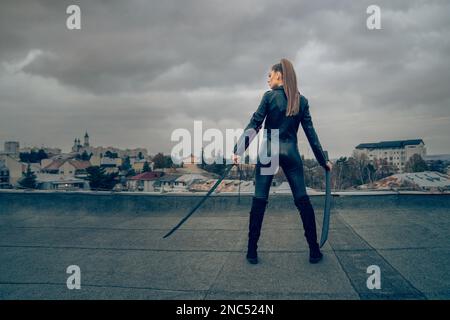 Vue arrière d'une femme nainja dans un ensemble en cuir qui porte deux épées japonaises Banque D'Images