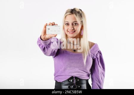Jeune femme souriante confiante portant un chemisier côtelé isolé sur fond blanc tenant une carte de crédit et montrant à l'appareil photo, à vous, et Banque D'Images