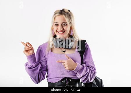 Jolie femme millénaire portant un chemisier isolé sur fond blanc excitée, avec un sac à dos et un casque autour du cou regarde la caméra A. Banque D'Images