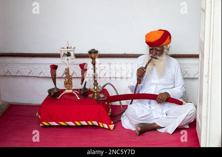 Jodhpur, Rajasthan, Inde - 19 octobre 2019 : Rajput homme âgé fumant à travers un narguilé, portant Marathi pagri et épée sur les genoux. Banque D'Images