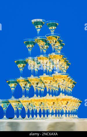 Verres à champagne debout dans la tour, fête festive. Pyramide de verres de cocktails, vin sur fond bleu Banque D'Images