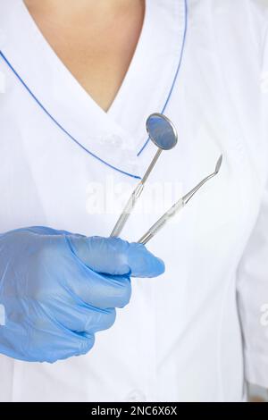 Vue rognée du dentiste dans un gant en latex tenant le dentiste outil professionnel près de l'ensemble dentaire flou sur les médecins manteau fond uniforme Banque D'Images