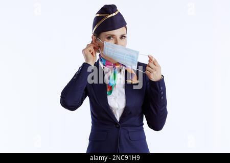 femme élégante d'hôtesse d'air sur fond blanc en uniforme portant un masque médical. Banque D'Images