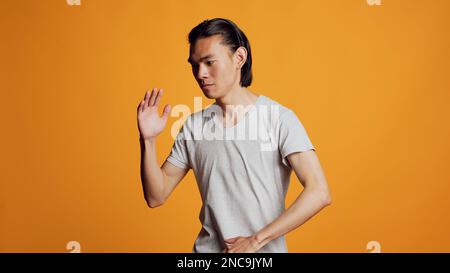 Personne positive montrant la danse robotique se déplace sur la caméra, agissant sily comme le robot sur fond orange. Joyeux homme insouciant dansant avec de l'énergie drôle en studio, danseur funky actif. Banque D'Images