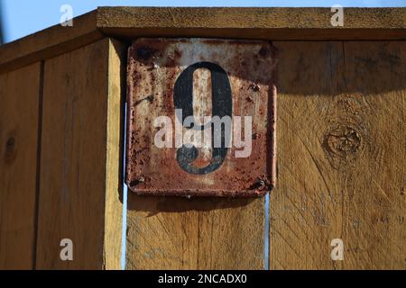 maison numéro 9 clôture en bois jaune avec un panneau d'adresse en métal, vieux rustique brun altéré fond, noir numéro neuf chiffres Banque D'Images