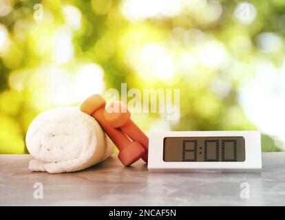 Horloge numérique, serviette et haltères sur table en marbre à l'extérieur. Exercice du matin Banque D'Images