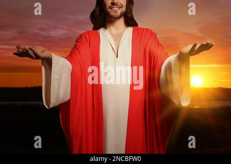 Jésus-Christ avec les bras étirés dehors au coucher du soleil Banque D'Images