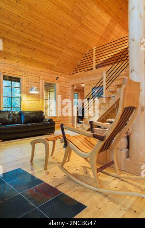 Fauteuil à bascule en bois et canapé en cuir brun dans la salle de séjour à l'intérieur de la maison en rondins de pin Scots, Québec, Canada. Cette image est la propriété validée Banque D'Images