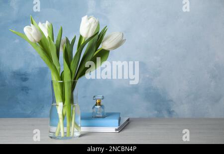 Magnifiques tulipes blanches, carnets et parfum sur table en bois sur fond bleu clair, espace pour le texte Banque D'Images