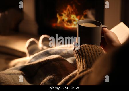 Femme avec une tasse de boisson près d'une cheminée à la maison, à proximité Banque D'Images