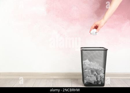 Femme jetant une boule de papier froissé dans le panier près du mur rose, gros plan. Espace pour le texte Banque D'Images