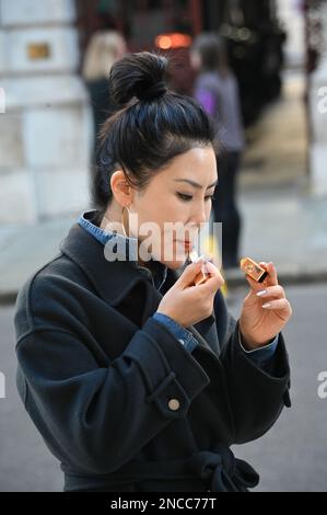 14th février 2023. Londres, Royaume-Uni. Une femme asiatique mettant un rouge à lèvres à Whitehall, Londres, Royaume-Uni. Banque D'Images