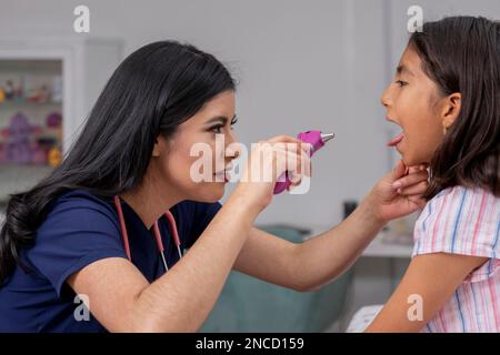 pédiatre féminin vérifiant la bouche d'un enfant dans son bureau avec une lampe Banque D'Images