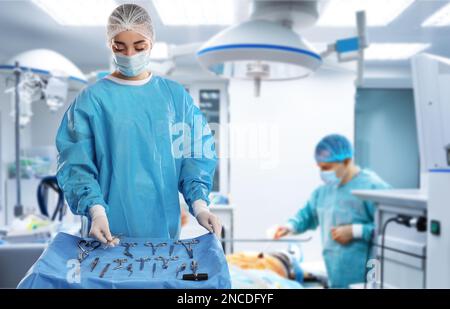 Infirmière près de la table avec différents instruments chirurgicaux dans la salle d'opération Banque D'Images