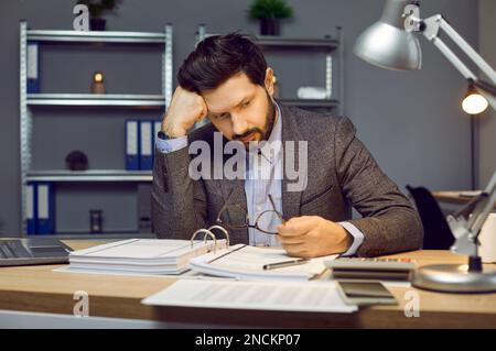 Portrait de frustré, réfléchi, barbu jeune homme de comptable ou d'entrepreneur assis dans le bureau à son lieu de travail avec un grand dossier de Banque D'Images