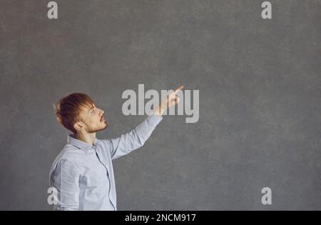 Photo de profil de côté de l'homme beau avec le doigt d'index de copyspace droit dans la publicité portant chemise bleue Banque D'Images