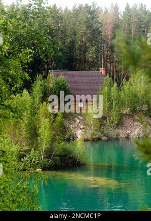 Maison en bois avec un plat satellite debout dans les bois dans les pins sur les rives du lac de pierre avec l'île et l'eau turquoise. Banque D'Images