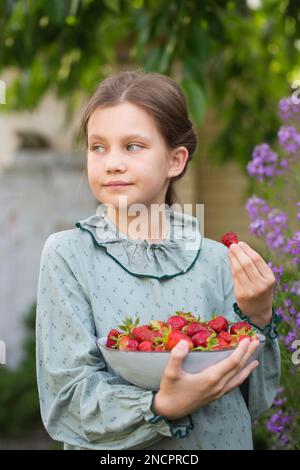 Jolie petite fille dans une robe vintage avec un bol de fraises mûres dans le jardin Banque D'Images