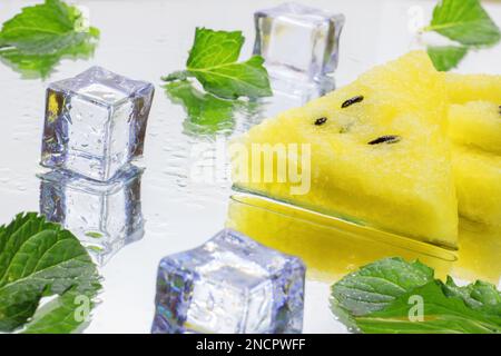 gros plan de quelques morceaux de pastèque rafraîchissante sur fond blanc, pastèque jaune avec feuilles de menthe et morceaux de glace, nourriture Banque D'Images