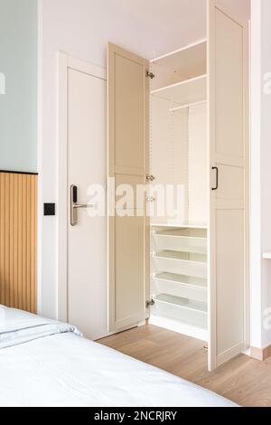 armoire en bois intégrée avec portes ouvertes beige. À l'intérieur de l'armoire, toutes les étagères, tiroirs et barres transversales sont en plastique blanc durable. Entrée à Banque D'Images