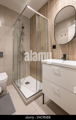 Salle de bains avec grande douche dans le coin. Lavabo rectangulaire sur table de toilette avec tiroirs blancs et miroir sur le mur avec cadre en métal noir. Murs Banque D'Images