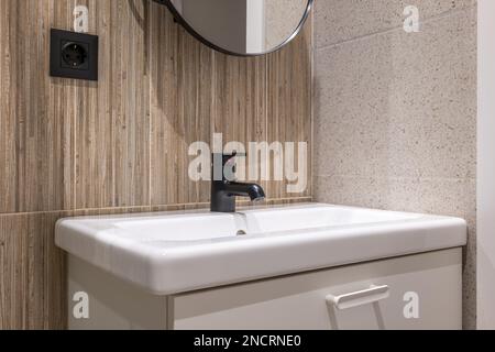 Le lavabo de la salle de bains est éclairé par la lumière du plafond. Les murs sont une combinaison de carreaux de granit gris et de marbre de grain de bois. Au-dessus de l'évier est Banque D'Images