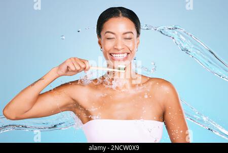 Brosse à dents en bambou de femme noire isolée sur fond bleu avec du dentifrice, des éclaboussures d'eau et la santé dentaire. Modèle ou personne se brossant les dents avec ECO Banque D'Images