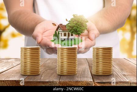 Pile de pièces de monnaie sur table en bois et homme tenant le modèle de maison. Investissement immobilier Banque D'Images