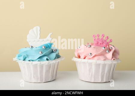 Délicieux petits gâteaux à la crème rose et bleu clair pour la douche de bébé sur table blanche Banque D'Images