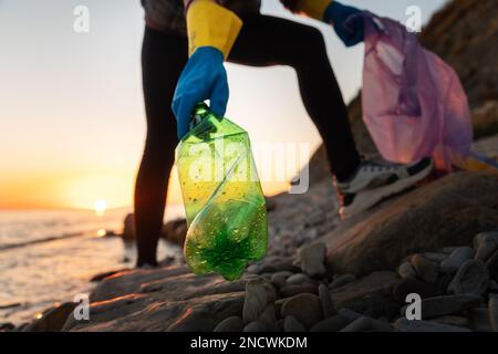Nettoyage côtier. Un volontaire doit ramasser une bouteille en plastique et tenir un sac à ordures, vue du dessous. Le concept de pollution environnementale et de conservation de Banque D'Images