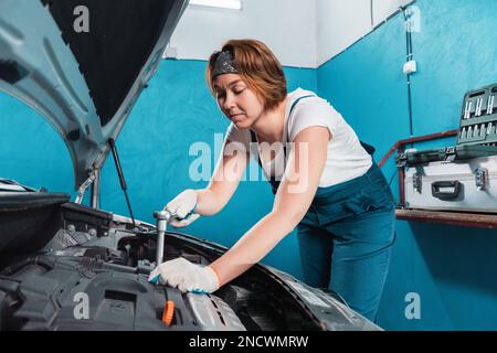 Mécanicien femme en combinaison réparer un moteur avec clé à cliquet. Le concept de l'égalité de la femme et travaille à l'atelier de réparation automobile. Banque D'Images