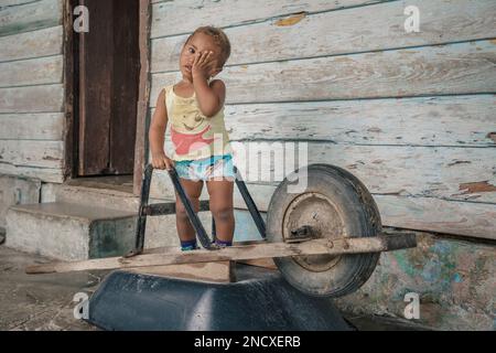 Augusto César Sandino, Artemisa, Cuba. 11 juillet 2019. Tout-petit jouant avec une brouette dans la porte de sa maison située dans une ville de campagne, Cuba. Banque D'Images