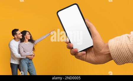 Joyeux couple arabe pointant vers le smartphone Big Blank dans la main féminine géante Banque D'Images