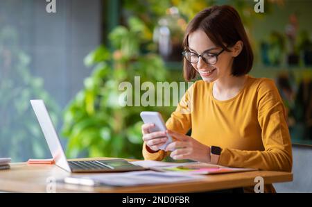 Jolie jeune femme utilisant un ordinateur portable et un smartphone au café Banque D'Images