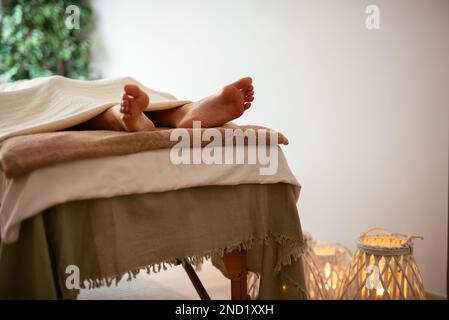 Crop unreconnaissables barefooted femme client allongé sur la table de massage sous la couverture pendant l'aromathérapie et la séance de réadaptation dans le salon de spa Banque D'Images