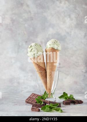 De délicieuses glaces sont servies dans des cornets de gaufres avec des feuilles de menthe fraîche et du chocolat placés dans un vase en verre sur fond gris Banque D'Images