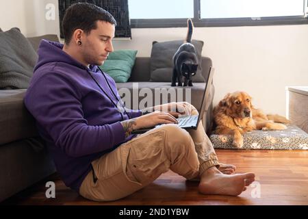 Tout le corps d'un travailleur indépendant concentré travaillant sur un ordinateur portable tout en étant assis sur le sol près de l'adorable chien Golden Retriever et du chat noir pendant le travail à distance Banque D'Images