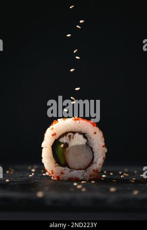 Délicieux sushi roulés avec de l'avocat et du fromage placés sur une surface sombre et servis avec du sésame Banque D'Images