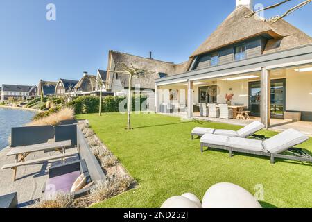 Bâtiment contemporain avec salle à manger sur terrasse et chaises longues sur pelouse verte près de la rivière dans le quartier de campagne Banque D'Images
