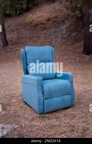 Confortable fauteuil bleu clair placé sur le sol dans la forêt d'automne avec des arbres verts et des feuilles mortes Banque D'Images
