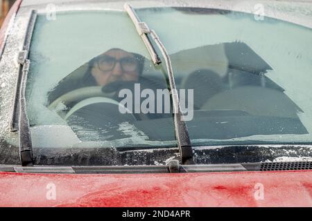 Gros plan d'un pare-brise de voiture gelé partiellement dégagé avec un conducteur mâle assis à l'intérieur. ROYAUME-UNI Banque D'Images