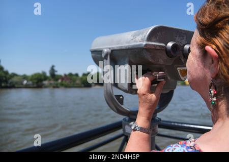 Femme latine mature regardant à travers des jumelles publiques sur la rive de la rivière Lujan à Tigre, Buenos Aires, Argentine. Banque D'Images