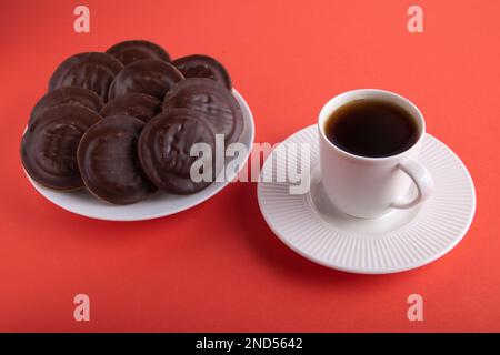 petits gâteaux enrobés de chocolat sur une assiette à côté d'une tasse de café chaud sur un fond coloré Banque D'Images