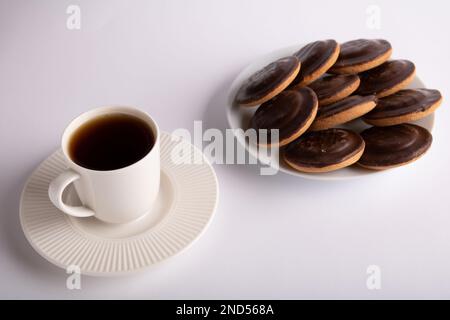 Les biscuits sont recouverts de chocolat sur le dessus et il y a une tasse de café sur un fond blanc sur une assiette Banque D'Images