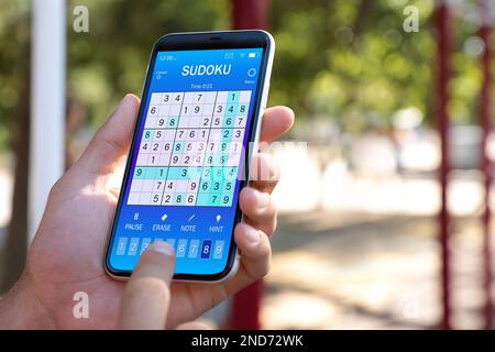 Homme jouant au jeu de sudoku sur smartphone en plein air, gros plan Banque D'Images