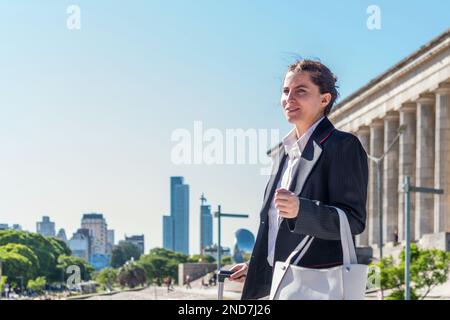 Femme d'affaires tenant un sac à main et tirant une valise tout en marchant à l'extérieur. Banque D'Images