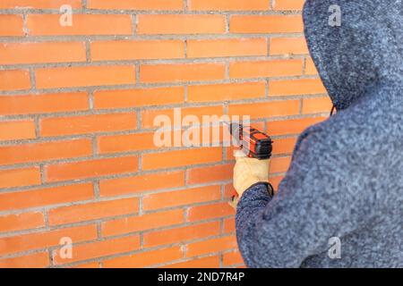 Homme sur son dos faisant des trous avec un exercice électrique dans le mur de brique. Banque D'Images