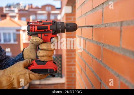 Foreuse avec batterie faisant des trous dans un mur de briques à l'extérieur. Banque D'Images